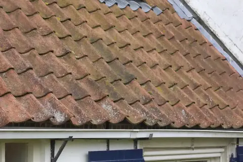 Tegole rosse consumate dal tempo, con muschio e licheni, suggeriscono la necessità di come sistemare un vecchio tetto per proteggere la casa.