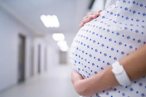 Brzuch kobiety w szpitalnej koszuli w niebieskie wzory, ręka na nim. Stan przedrzucawkowy.