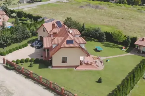 Piękny dom z ogrodem, gdzie mieszka Skolim. Widać panele słoneczne, dwa samochody i plac zabaw.