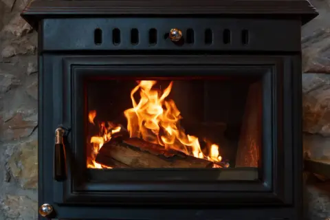 Un feu crépite dans un poêle à bois, le branchement poele a bois est discret derrière la pierre.