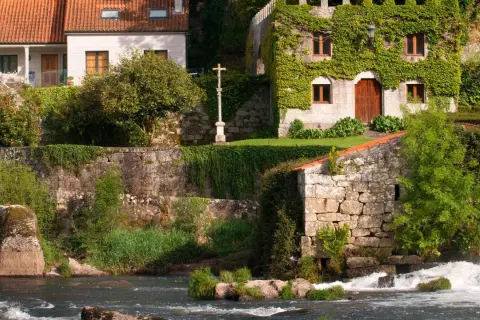 El pazo de Ponte Maceira, con su arquitectura de piedra y vegetación exuberante, se alza junto a un río de aguas bravas.