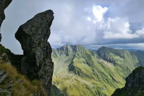 Steile Felsformationen und grüne Berghänge im Rahmen einer **Karpaten Wanderung**. Dramatische Wolkenformationen über den Gipfeln.