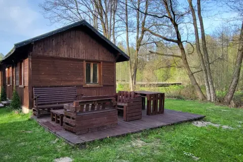 Drewniana chata z meblami na tarasie, otoczona zielenią i lasem. Idealne miejsce na agroturystykę w pobliżu.