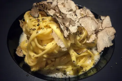 Tagliatelle al tartufo, un piatto elegante con pasta fresca condita con una cremosa salsa e generosamente guarnita con scaglie di tartufo nero.