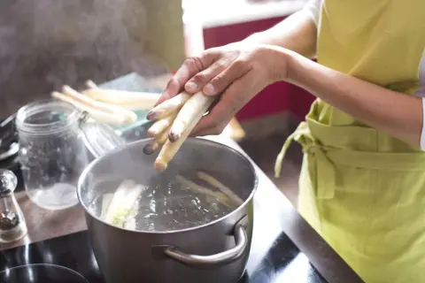 Hände legen weißen Spargel in kochendes Wasser. So wird gefrorener Spargel kochen.