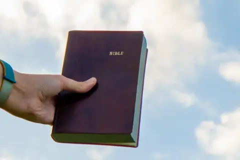 Dłoń trzyma Biblię na tle nieba. Czy to znaczy "Deus Deus Kosmateus"?