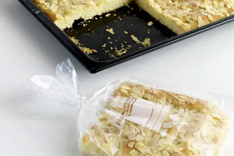 Ein Stück Mandelkuchen ist in einer Plastiktüte verpackt, bereit zum Kuchen einfrieren. Daneben liegt die Backform mit den restlichen Stücken.