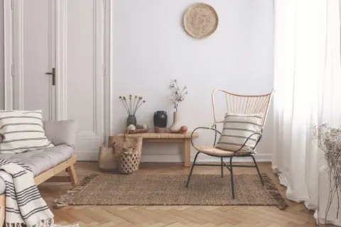 Un angolo del salotto arredato con un divanetto in legno, una poltrona in rattan, tappeto in juta e decorazioni naturali. Ecco come riempire un angolo del salotto con stile.