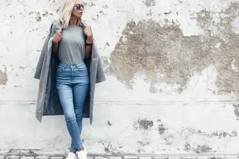 Modelka w jasnych jeansach skinny i szarym płaszczu. Dowiedz się, jakie jeansy do jakiej figury pasują najlepiej.
