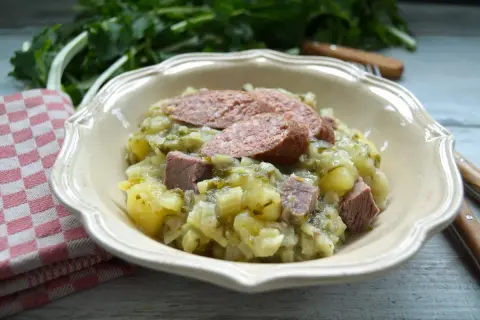 Herzhaftes Stielmus mit Kartoffeln und Wurst in einer Schüssel, daneben ein kariertes Tuch.