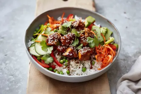 Pyszny bowl z kurczakiem w sosie teriyaki, ryżem, chrupiącą marchewką, ogórkiem, groszkiem i papryką.