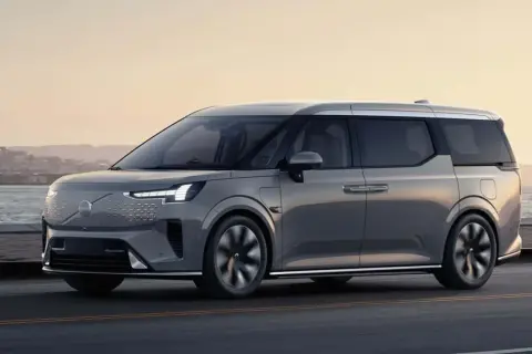 Elegancki, szary minivan Volvo EM90 jedzie wzdłuż wybrzeża o zachodzie słońca.