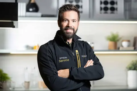 Uśmiechnięty serwisant Whirlpool w czarnej kurtce z napisem "Official Service". Pomoże Ci z instrukcją obsługi pralki Whirlpool.