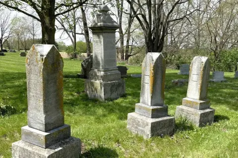 Vieilles pierres tombales dans un cimetière verdoyant, sous des arbres feuillus. Un lieu paisible pour se souvenir.