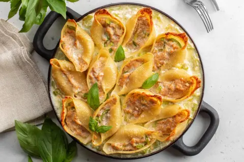Un plat de conchiglioni farcis, dorés et garnis d'une farce savoureuse, baignant dans une sauce crémeuse et décorés de feuilles de basilic frais.