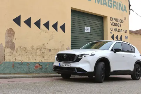 Vit Mazda CX-5 framför en sliten gul byggnad med svarta pilar. Kanske ett Mazda CX-5 problem med att hitta rätt väg?