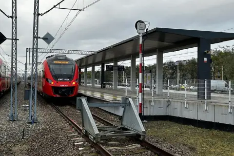 Czerwony pociąg PKP SKM stoi na peronie. W tle nowoczesna wiata i słup sygnalizacyjny.