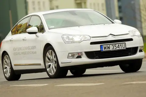 Biały Citroen C5 2.0 HDi z napisem "NOWY SILNIK 3.0 V6 HDi 240KM" na drzwiach, jadący po drodze.