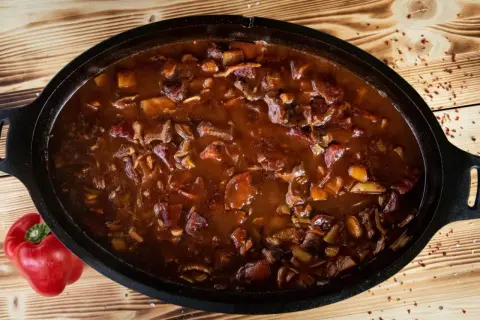 Herzhaftes Gulasch im Dutch Oven, perfekt für rustikale Dutch Oven Rezepte. Daneben liegt eine rote Paprika.