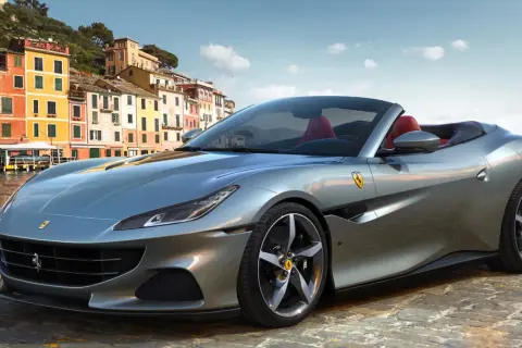 Srebrny Ferrari Portofino z czerwonym wnętrzem na tle kolorowych budynków nad wodą.