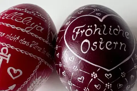 Zwei bemalte Ostereier: Ein rotes mit "Halleluja" und Anker, ein dunkles mit "Fröhliche Ostern" und Herzen. Ein schöner risus paschalis.