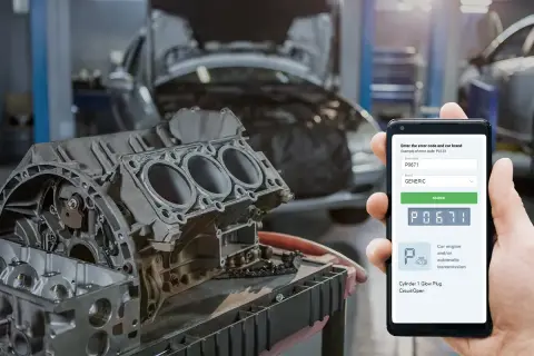Mechanik sprawdza kod błędu dtc p0671 Opel na telefonie, obok rozebranego silnika w warsztacie.