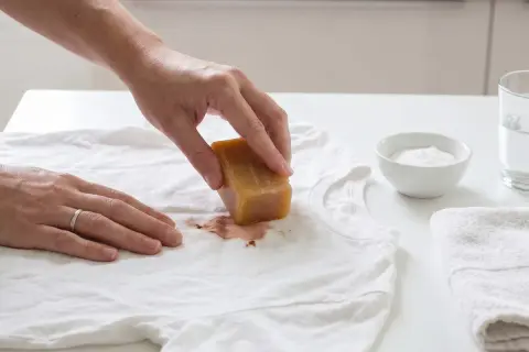 Hand reibt mit Kernseife über Blutfleck auf weißem T-Shirt. So lässt sich blut aus kleidung entfernen.