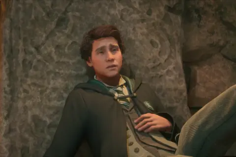 Zamyślony Sebastian z Hogwarts Legacy opiera się o kamień, w szacie Slytherinu.