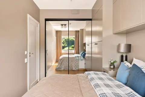 Ein großer spiegel im schlafzimmer reflektiert das Bett, die Vorhänge und das Fenster mit Blick ins Grüne.