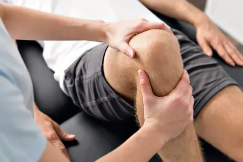 Physiotherapeut untersucht das Knie eines Mannes, um Probleme mit dem hinteren Kreuzband zu identifizieren.