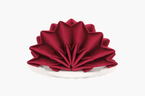 Pliage serviette tissu noël en forme d'étoile, rouge profond, sur une assiette blanche. Une touche festive pour votre table.