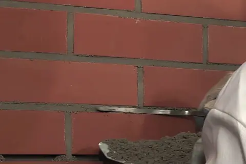 Pracownik nakłada fugę do klinkieru na ceglaną ścianę za pomocą kielni.