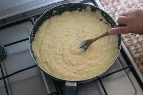Masa de croquetas cremosa en sartén, removida con cuchara de madera.