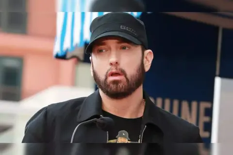 Eminem, znany jako "mockingbird po polsku", w czapce i z brodą, przemawia do mikrofonu.