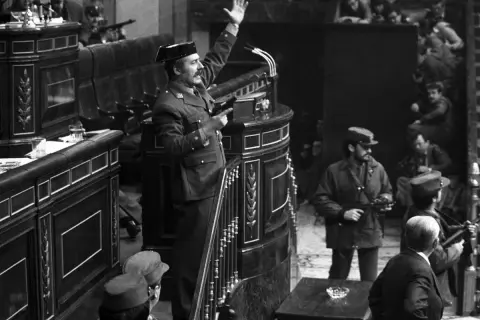 Un militar con pistola en mano, saludando, en el Congreso durante el golpe de estado de Tejero. Soldados armados observan.