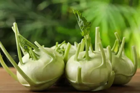 Mehrere kleine Kohlrabi-Knollen mit grünen Blättern liegen auf einem Holztisch.