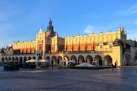 Sukiennice Kraków w blasku słońca, z arkadami i wieżą zegarową. Rynek tętni życiem.