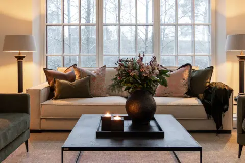 Mysig lounge med soffa och gröna artwood fåtöljer. Blommor, ljus och en filt skapar en varm atmosfär.