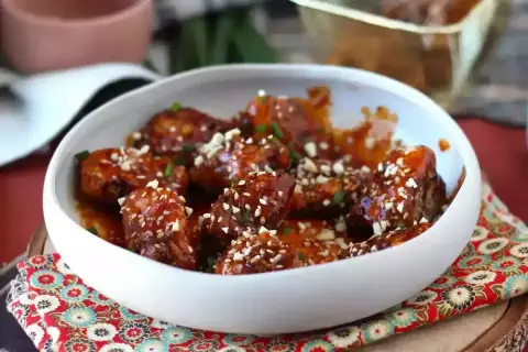 En skål med glaserade kycklingvingar, strödda med sesamfrön och hackade nötter. Perfekt för en festlig middag med goda وصفات دجاج.