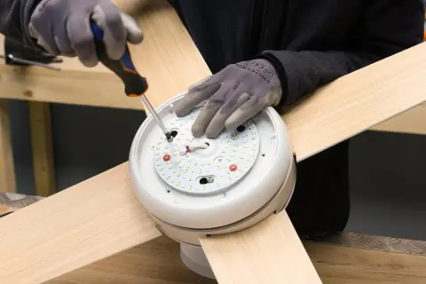 Manos enguantadas atornillan el motor de un ventilador de techo.
