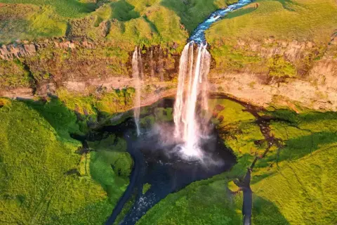 Wspaniały wodospad na Islandii latem. Zielone wzgórza i rwąca rzeka tworzą malowniczy krajobraz. Idealne miejsce, by zobaczyć, co Islandia ma do zaoferowania.