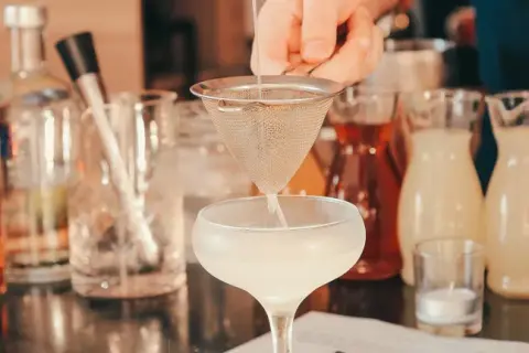 Barman przygotowuje drinka, obok stoją butelki z różnymi alkoholami i syropami. Idealny wybór, jaki alkohol na wesele, by zadowolić wszystkich gości.