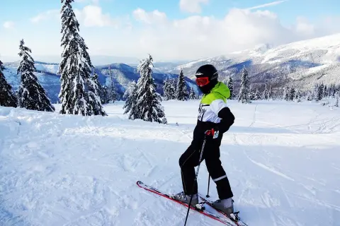 Narciarz na łagodnych stokach narciarskich Zakopane dla początkujących, otoczony ośnieżonymi drzewami i górami.