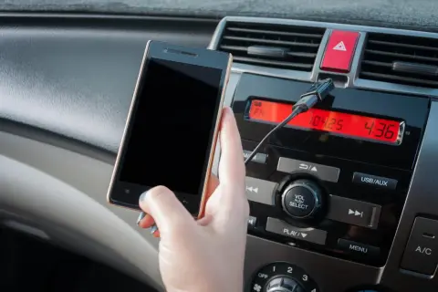 Ręka trzyma smartfon, podłączony kablem do radia samochodowego. Dowiedz się, jak połączyć się z transmiterem.