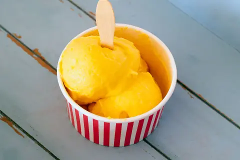 Un refrescante helado de mango en un recipiente a rayas rojas y blancas, listo para disfrutar en un día caluroso.