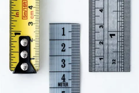 Tre metri diversi mostrano come si misura il tacco di una scarpa: uno giallo con indicazioni in pollici e centimetri, uno azzurro con numeri grandi e uno metallico con tacche precise.