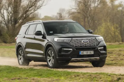 Czarny Ford Explorer 4x4 pokonuje piaszczystą drogę wśród jesiennej przyrody.