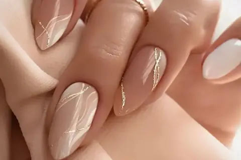 Elegancki, modny manicure w odcieniach beżu i bieli, ozdobiony złotymi, falistymi liniami.