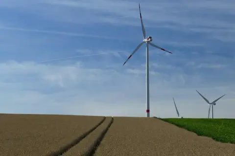 Wiatrak na polu zbożowym, z innymi wiatrakami w tle, pod błękitnym niebem z chmurami.