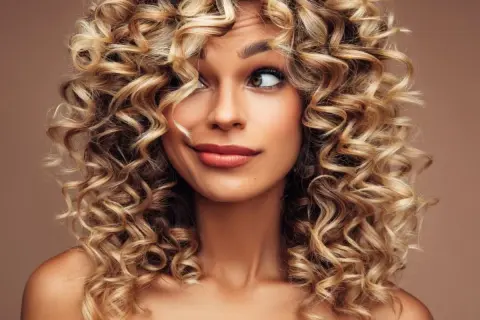 Kobieta z burzą blond loków do ramion. Jej fryzury włosy kręcone do ramion dodają jej uroku.